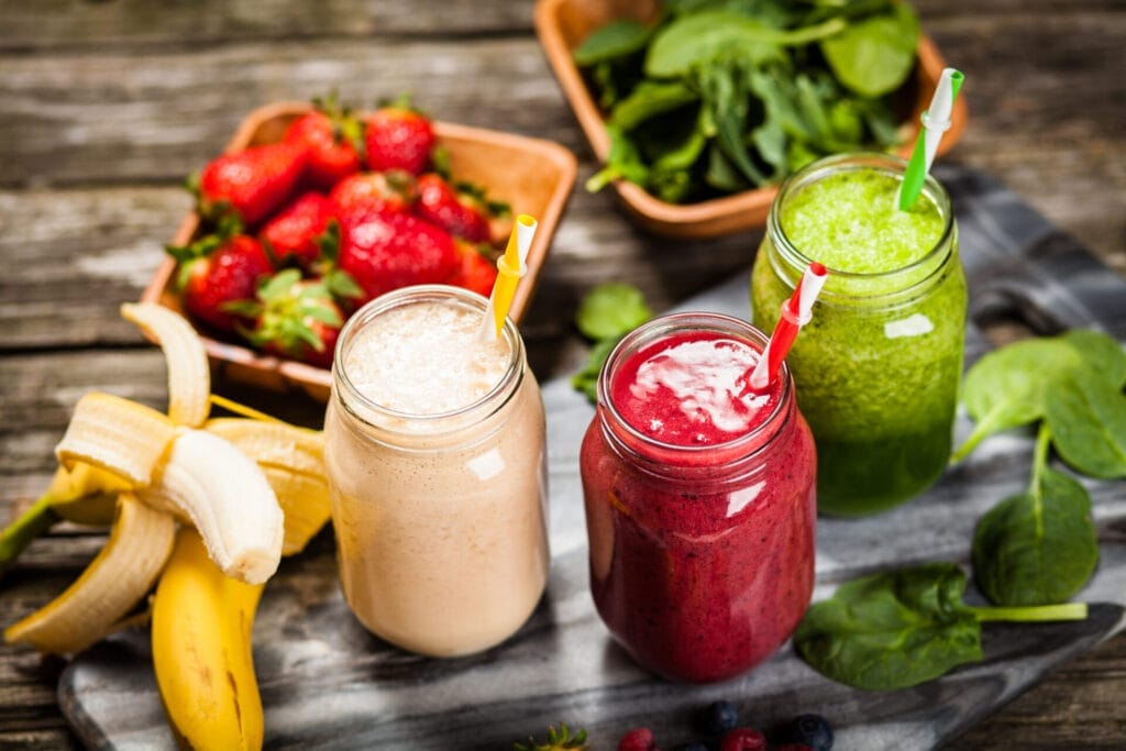 Assortment of smoothies surrounded by fruits and vegetables on wooden table.