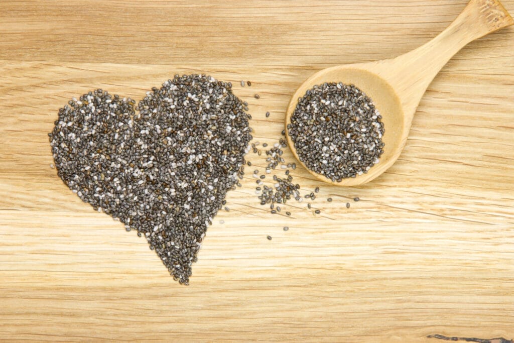 Wooden spoon filled with black chia seeds and heart symbol, on a light wooden background.
