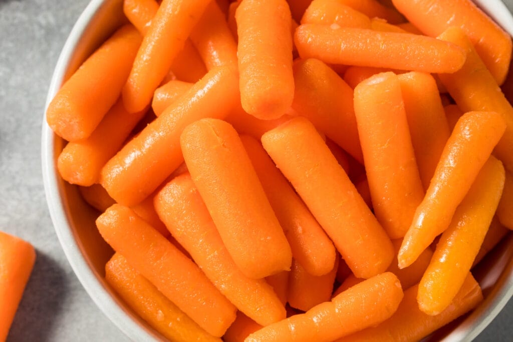 Baby carrots in a white bowl on gray background.